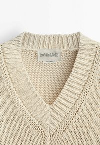 Pull en maille beige avec un col en V, présentant un col côtelé et une texture ample. L'étiquette indique "Massimo Dutti Édition Limitée."