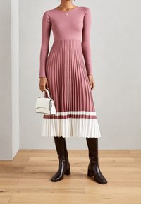 Vaaleanpunainen pitkähihaisella mekko, jossa on laskostettu hame ja valkoisia sekä viininpunaisia raitoja helmassa. Yhdistetty polvipitkiin mustiin saappaisiin ja valkoiseen käsilaukkuun.