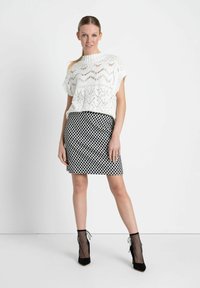 Haut tricoté blanc à manches courtes avec un motif en chevrons, associé à une jupe à pois noir et blanc et des bottines à filets noires.