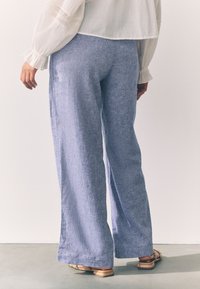 Hele sinised, laiade säärega püksid, mis on valmistatud tekstuurse kangaga. Omavad lahtist lõiget ja sirget ääreosa. Kandmisel helepruunid madalad sandaalid.