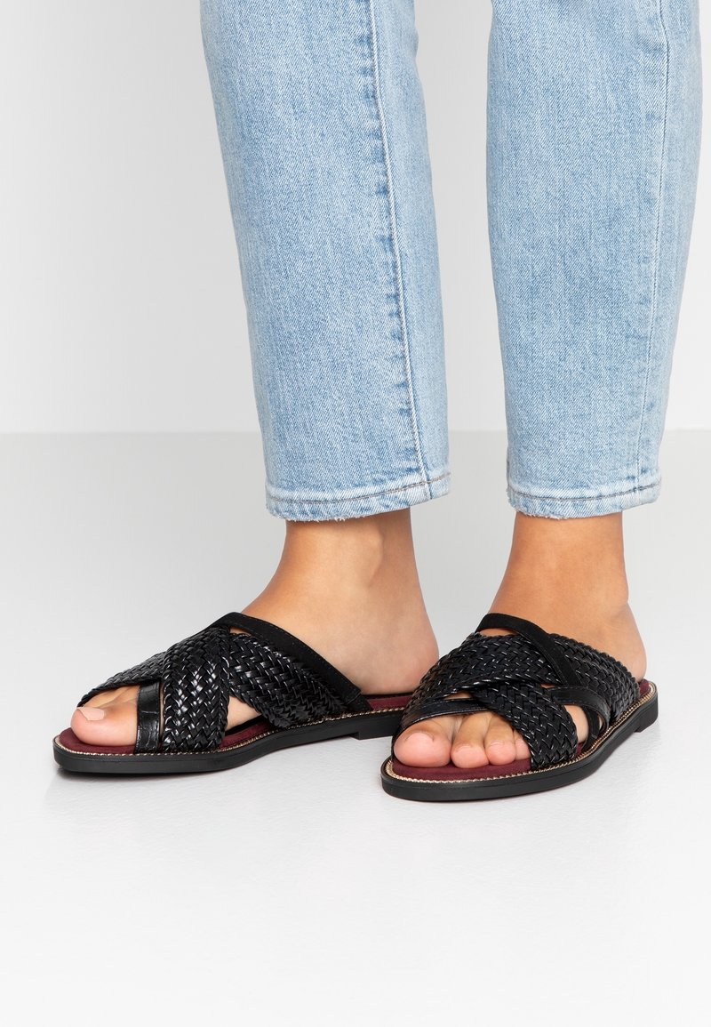Sandales glissantes noires tissées avec une conception à bout ouvert, dotées de brides texturées et d'une semelle plate avec un accent bordeaux contrastant.