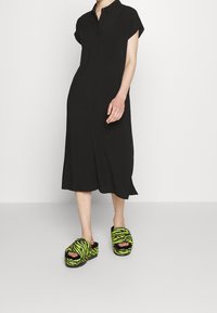 Czarna sukienka na guziki z krótkimi rękawami, do kolan. W połączeniu z puszystymi, czarnymi klapkami w neony zielone paski tygrysa. Gładka faktura materiału.