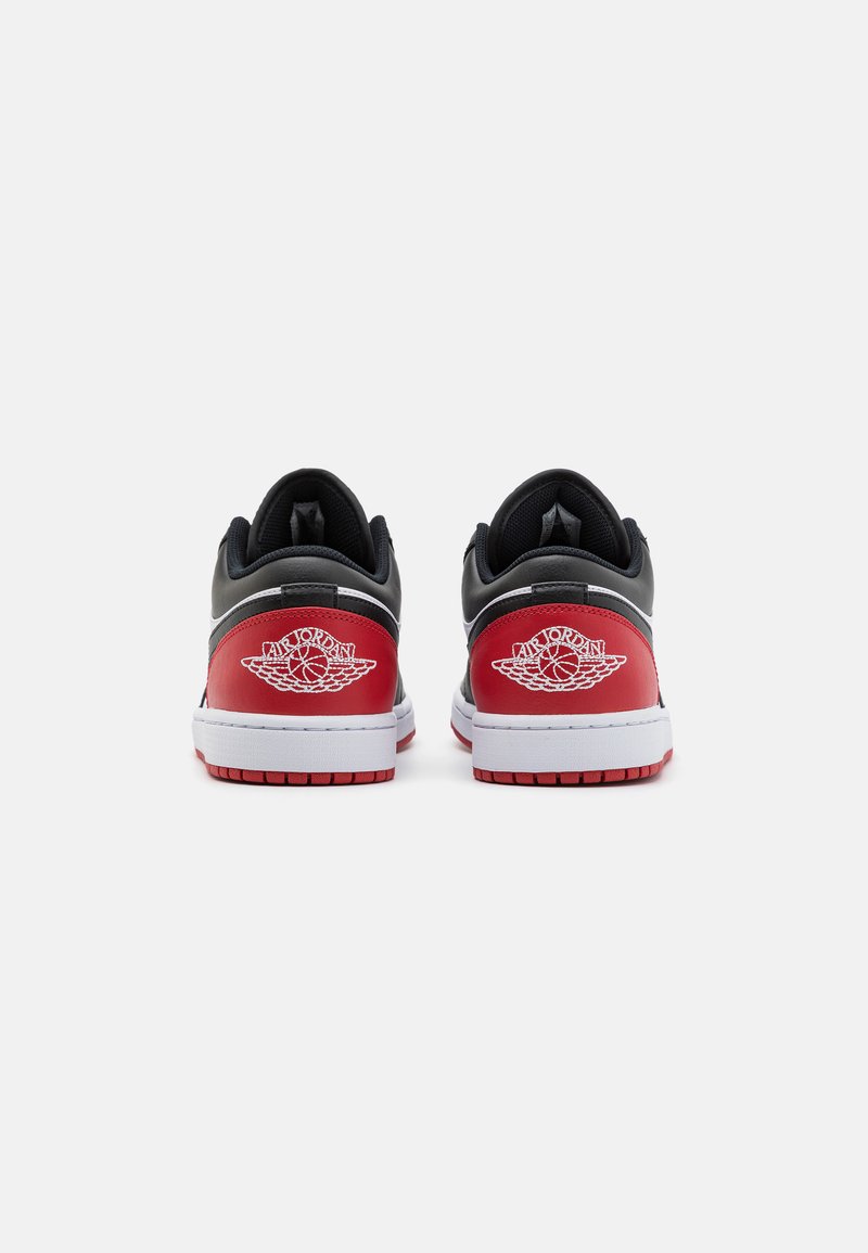 Schwarze und rote Sportschuhe mit einem glatten Lederoberteil, das eine weiße Sohle, auffällige Logodetails und strukturierte Akzente an der Ferse aufweist.