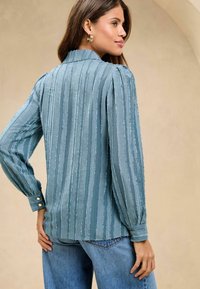 Lichtblauwe gestreepte blouse van een textuurstof, met lange mouwen, met knoopmanchetten en een klassieke kraag, gecombineerd met een hoge taille jeans.
