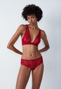 Completo in pizzo rosso composto da reggiseno e slip con motivi floreali, bordi scallop e un fiocco centrale sullo slip. Texture morbida e trasparente con coppe triangolari.