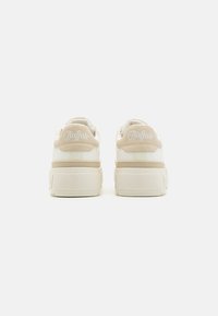 Beige és krém színű Buffalo márkájú sportcipők, texturált felsőrésszel, párnázott bokarészzel és vastag fehér talppal, hátul logo részlettel.