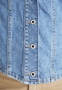 Svetlo modra denim srajca z kovinskimi gumbi ob placketu in vidnim šivanjem. Mehka tekstura z zasnovo v sproščenem kroju.