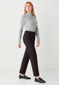 Haut gris à manches longues associé à un pantalon fuselé marron foncé avec poches latérales. Chaussures plates noires avec un détail de boucle décorative.