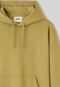 Sweat à capuche vert olive avec capuche à cordon de serrage, poignets côtelés, poche frontale et tissu doux et texturé. L'étiquette indique "Bzb."