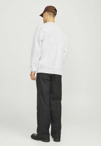 Felpa bianca con maniche lunghe, polsini e orlo a coste, abbinata a pantaloni neri e un cappello marrone. Struttura liscia, design informale.