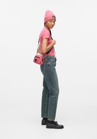 T-shirt aderente rosa, jeans dritti in lavaggio chiaro, mocassini neri e un berretto rosa. Una piccola borsa a tracolla rosa con un dettaglio zip.
