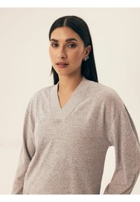 Jasnoszary sweter w serek wykonany z miękkiej dzianiny. Posiada długie rękawy i luźny krój. Minimalna tekstura z prążkowanym dekoltem.