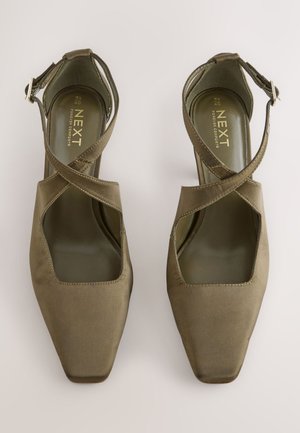 Olijfgroene satijnen pumps met hoge hak, een vierkante neus, open zijkanten en gekruiste enkelbandjes. De binnenkant heeft een gevoerde binnenzool.