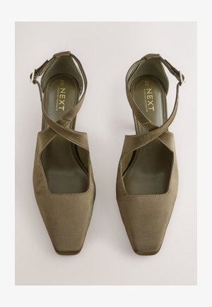 Satinové vysoké podpätky olivovo zelenej farby so štvorcovou špičkou, otvorenými stranami a prekríženými remienkami okolo členku. Vo vnútri majú mäkkú vložku.