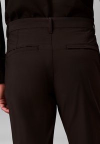Pantalones negros con textura suave, que cuentan con una cinturilla ajustada, dos bolsillos traseros y detalles de costuras limpias.
