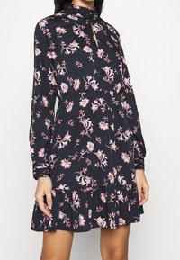 Long-sleeved dark floral dress with a high neck, featuring pink and white flowers. Ruffled hem and keyhole neckline add visual detail.