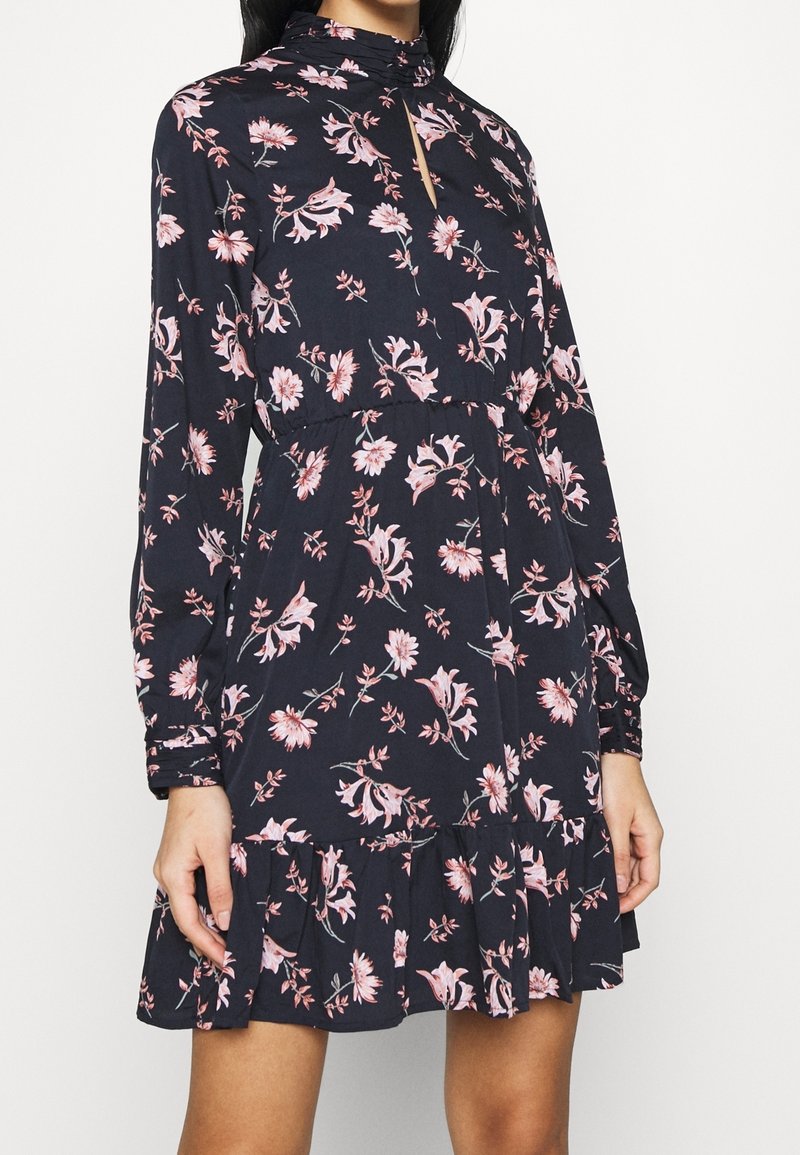 Long-sleeved dark floral dress with a high neck, featuring pink and white flowers. Ruffled hem and keyhole neckline add visual detail.