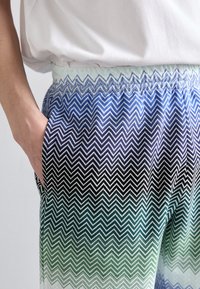 Pantaloni cu talie elastică, având un model în zigzag în nuanțe de albastru, negru și verde, cu o textură netedă și buzunare laterale.