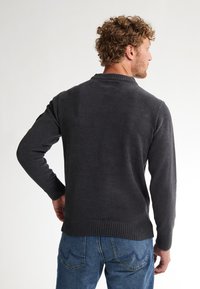 Pull en tricot gris avec un ourlet et des poignets à côtes, des manches longues et un col rond, associé à un jean bleu avec un design de couture courbée.