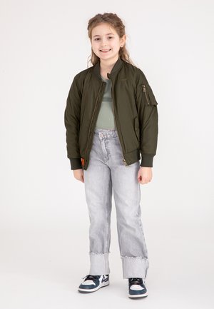 Olijfgroene bomberjack met ribgebreide manchetten, voorrits en patzak. Gecombineerd met lichtgrijze versleten jeans en zwarte sneakers.