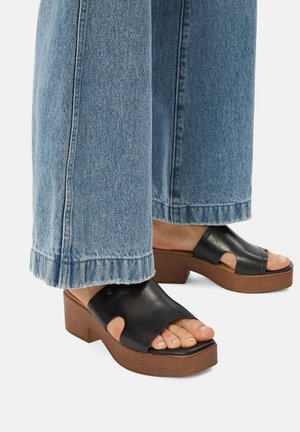 Črne usnjene platform sandale z odprtim prstom in stranskimi izrezi, kombinirane z svetlo modrimi širokimi kavbojkami z raztrganimi robovi.