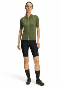 Maglia da ciclismo a maniche corte di colore verde oliva con cerniera anteriore e dettagli in verde neon, abbinata a pantaloni da ciclismo neri e calze nere.