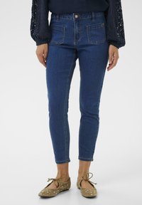 Siniset slim fit farkut korkealla vyötäröllä, joissa on etu- ja takataskut, viimeistelty hienovaraisilla ompelutiedoilla. Yhdistetty beigen koristellut balettitanut.