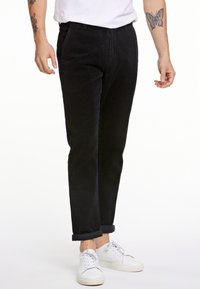 Pantalones de pana negros con corte recto, que cuentan con bolsillos y dobladillos enrollados, combinados con zapatillas blancas. La textura es acanalada.