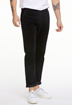 Pantalons en velours côtelé noirs avec une coupe droite, dotés de poches et d'ourlets roulés, associés à des baskets blanches. La texture est côtelée.