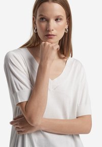 Maglione bianco con scollo a V e maniche corte a sbuffo, realizzato in tessuto morbido. Presenta dettagli di cucitura discreti e una vestibilità comoda.