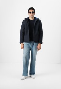 Navy hooded jacket with a blue interior, worn over a black sweater, paired with light blue flared jeans and white sneakers.