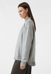 Szara bluza z okrągłym dekoltem, prążkowanymi mankietami oraz warstwowym dołem ozdobionym czarno-białymi paskami dla dodatkowego detalu.