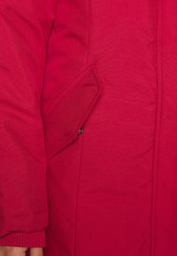 Czerwona pikowana kurtka z boczną kieszenią na klapkę. Tkanina ma gładką fakturę, a mankiet jest ściągany, co zapewnia dopasowanie.