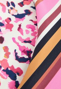 Textiel met een roze en blauwe luipaardprint naast brede horizontale strepen in mahonie, zwart, geel en blush op een zachte stof.