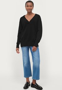 Sort strikket sweater med V-hals, ribbede manchetter og kant. Båret med lyseblå cropped jeans og sorte loafers. Glat og afslappet stil.