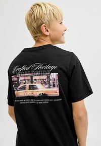 Czarna bawełniana koszulka z kolorowym miejskim nadrukiem z tyłu, z białym napisem "Crafted Heritage Worldwide Originals."