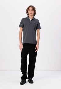 Grå polo-skjorte med lys grå krage, brukt med svarte vide bukser og svarte sko. Stoffet ser glatt ut med en klassisk passform.