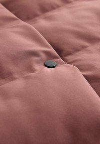 Bordo tikitud kangas sujuva tekstuuriga, mille keskel on silmapaistev must nupp. Peen sära täiustab disaini.