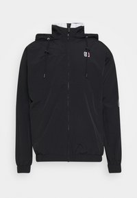 Chaqueta ligera negra con cierre de cremallera en la parte delantera, capucha ajustable, puños elásticos y detalle del logo en el pecho y la manga. Textura suave.