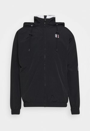 Chaqueta ligera negra con cierre de cremallera en la parte delantera, capucha ajustable, puños elásticos y detalle del logo en el pecho y la manga. Textura suave.