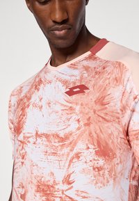 Camisa atlética de mangas curtas em coral e rosa claro, apresentando um design texturizado com padrões abstratos e um pequeno logótipo no peito.