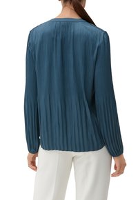 Blusa plissettata teal con maniche lunghe, scollatura rotonda e finitura testurizzata. Il retro è più lungo del davanti, con orlo dritto.