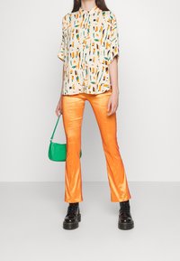 Short-sleeve shirt with a colorful abstract pattern, orange satin flared pants, and a green croc-embossed handbag. Black chunky boots.