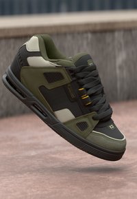 Green and gray sneaker with leather and textile upper, textured accents, padded collar, and black rubber sole. Features yellow eyelets and logo.