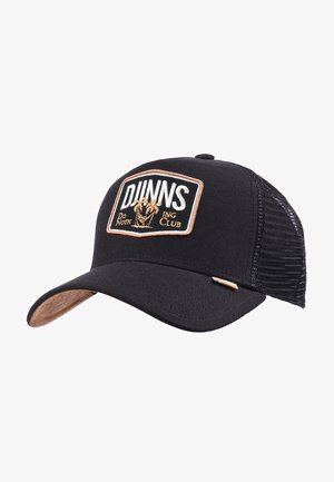 Black trucker cap with a mesh back, features a rectangular patch with "DJUNNS Do Noth ing Club" embroidered in white and gold. Flat brim.
