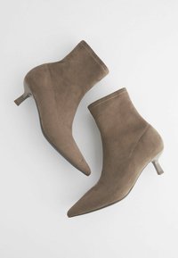 Bottines en daim taupe avec bouts pointus et petits talons aiguilles, présentées côte à côte sur un fond blanc.