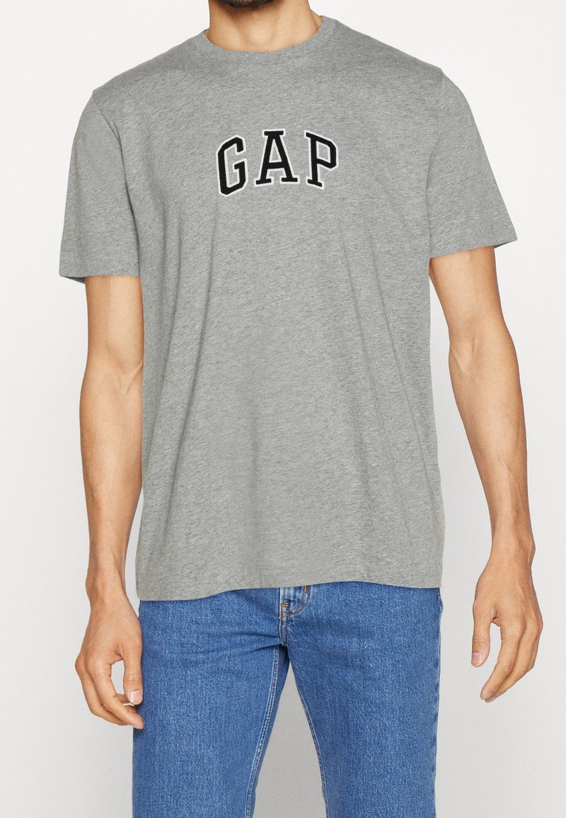 Camiseta de algodón gris con cuello redondo y mangas cortas, con la palabra "GAP" en letras negras y en negrita en el pecho.