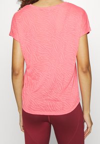 Różowy top z krótkim rękawem z subtelną fakturą zebry, odkrytym okrągłym dekoltem i zaokrąglonym dołem, w komplecie z bordowymi legginsami.