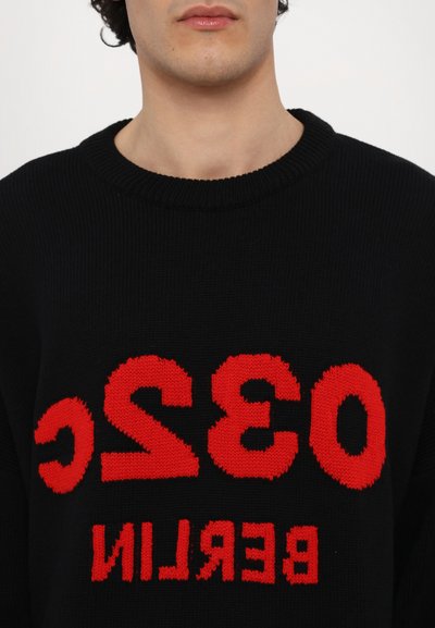Czarny sweter z dzianiny z wyraźnym czerwonym napisem "032 BERLIN" z przodu. Zaprojektowany z klasycznym okrągłym dekoltem i prążkowanymi detalami.