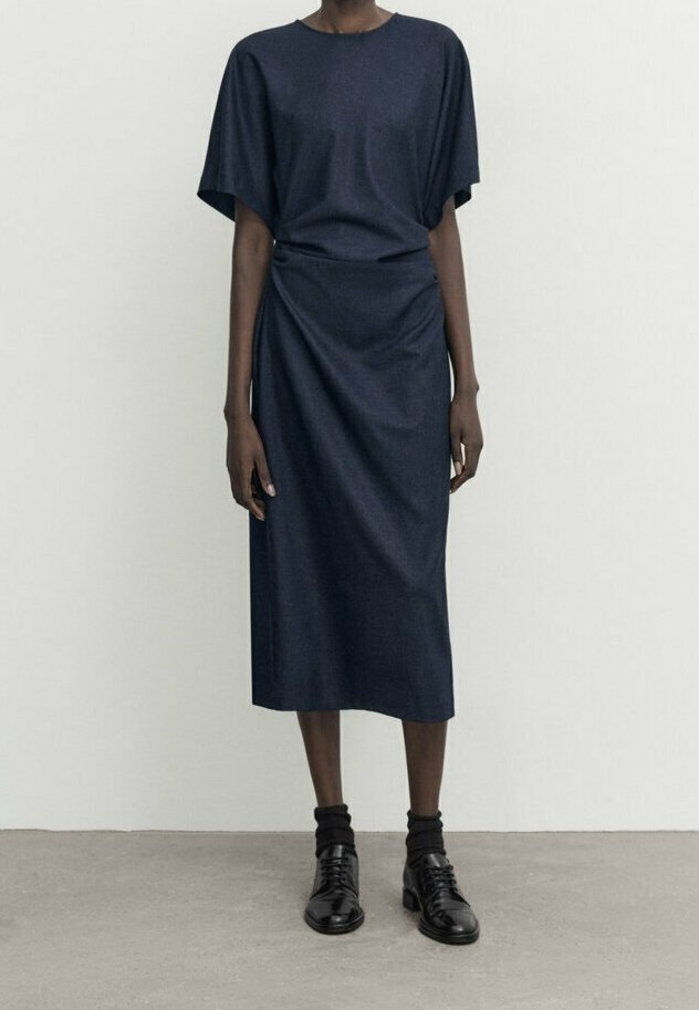 Navyblaues Kleid mit lockerer Passform, kurzen Ärmeln und asymmetrischem Drapé-Design. Mit glattem Stoff und knielangem Schnitt. Kombiniert mit schwarzen Schuhen.